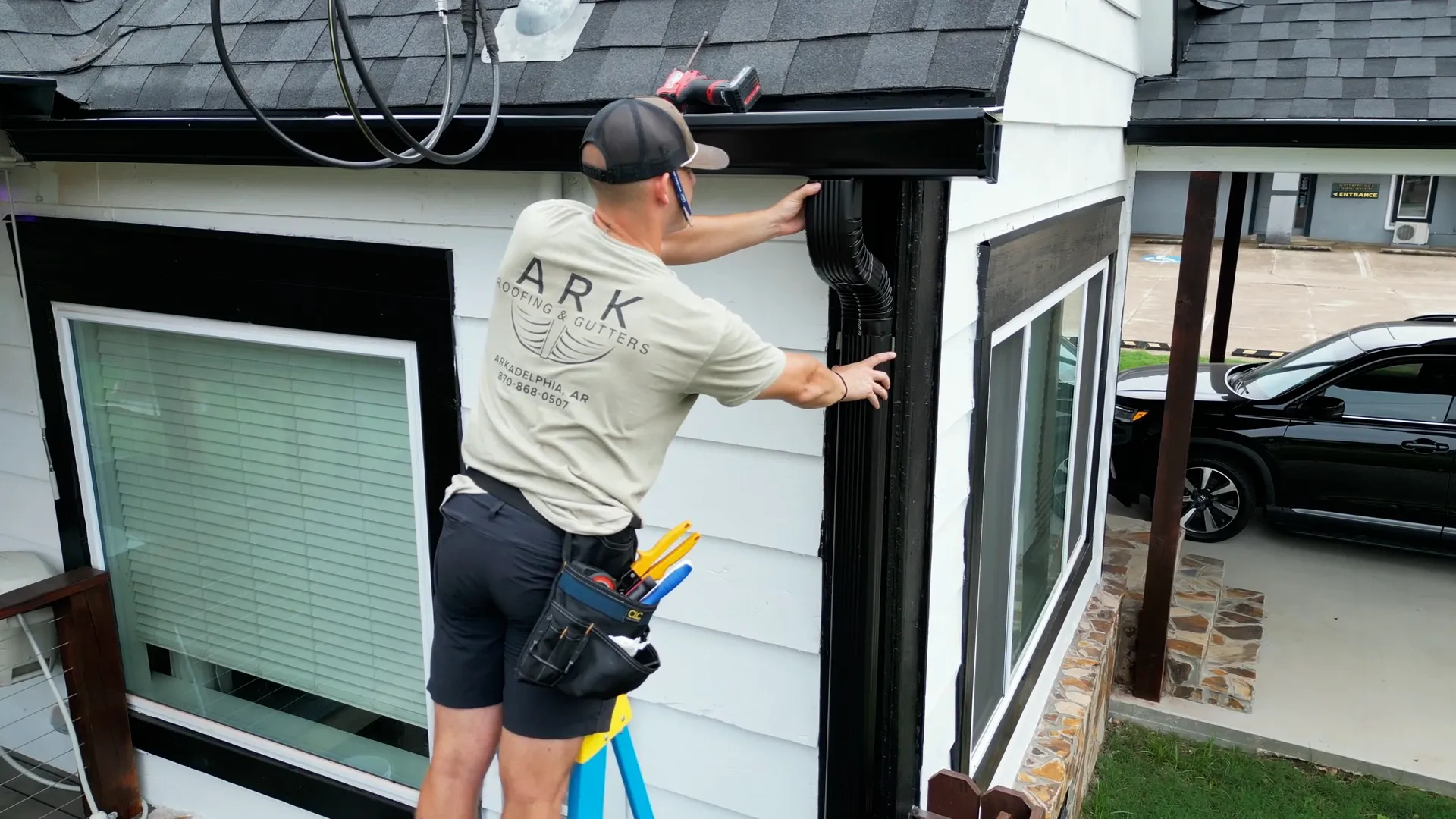 Installer refitting a torn-loose downspout section back under the gutter at a house corner