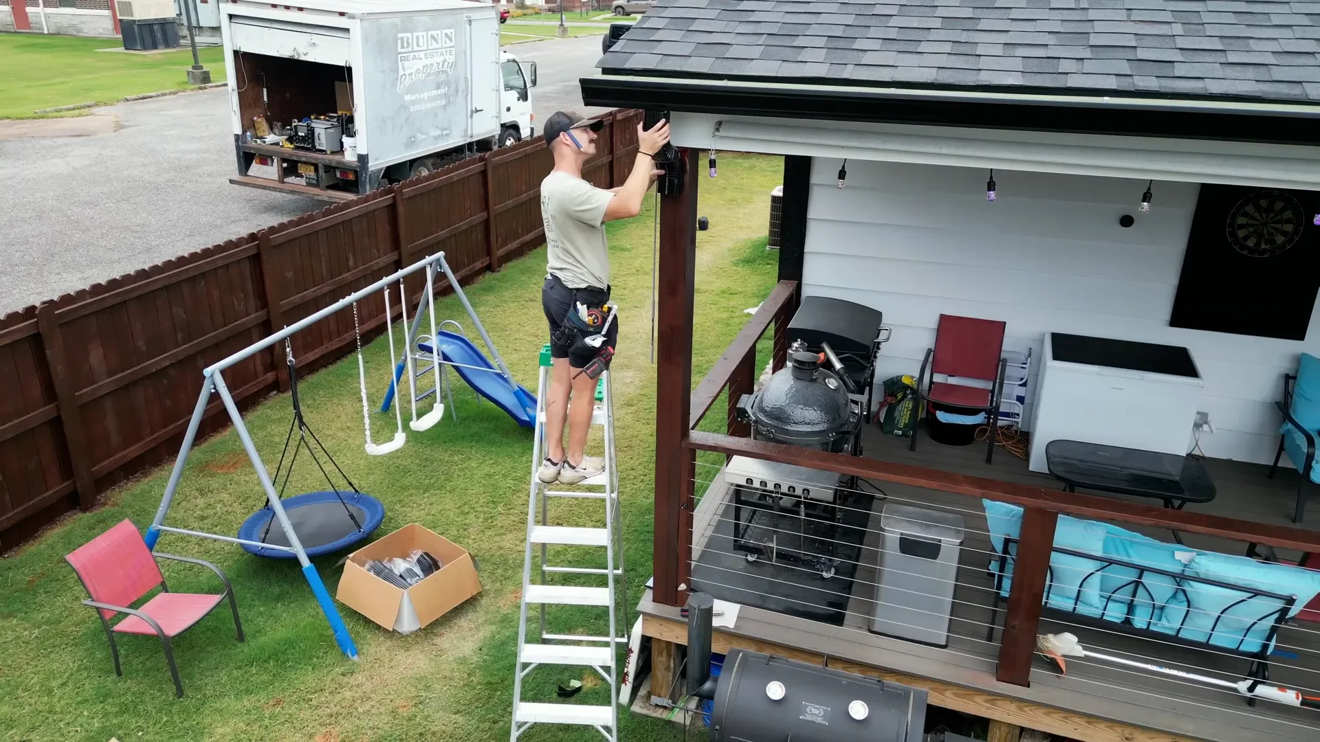 Ark Roofing installer raising a new black downspout section to the eave on gutter installation day