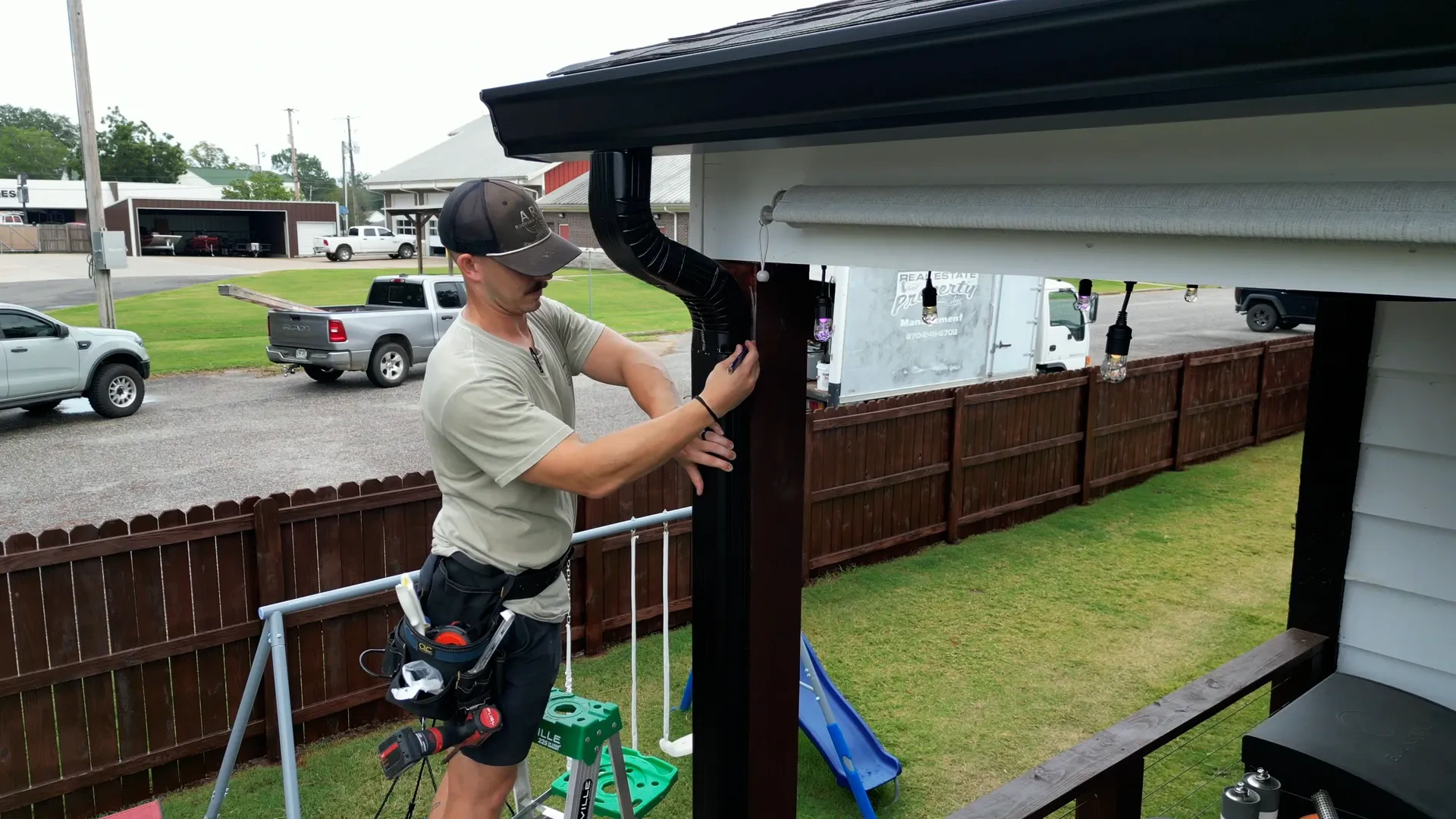 Installer joining a black downspout elbow to the drop outlet under a new gutter run