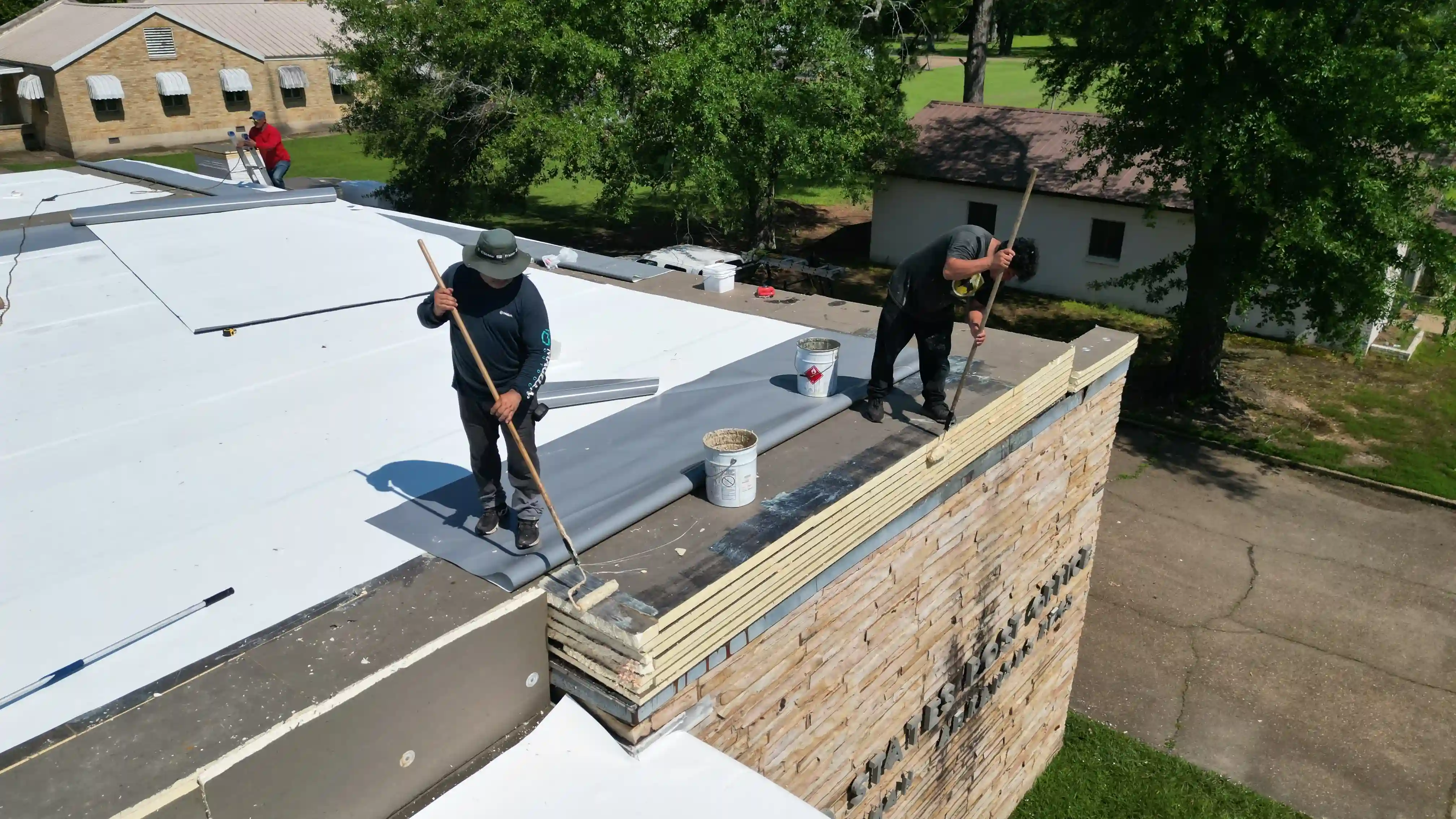 Crew applying white membrane along a parapet wall on a flat commercial roof