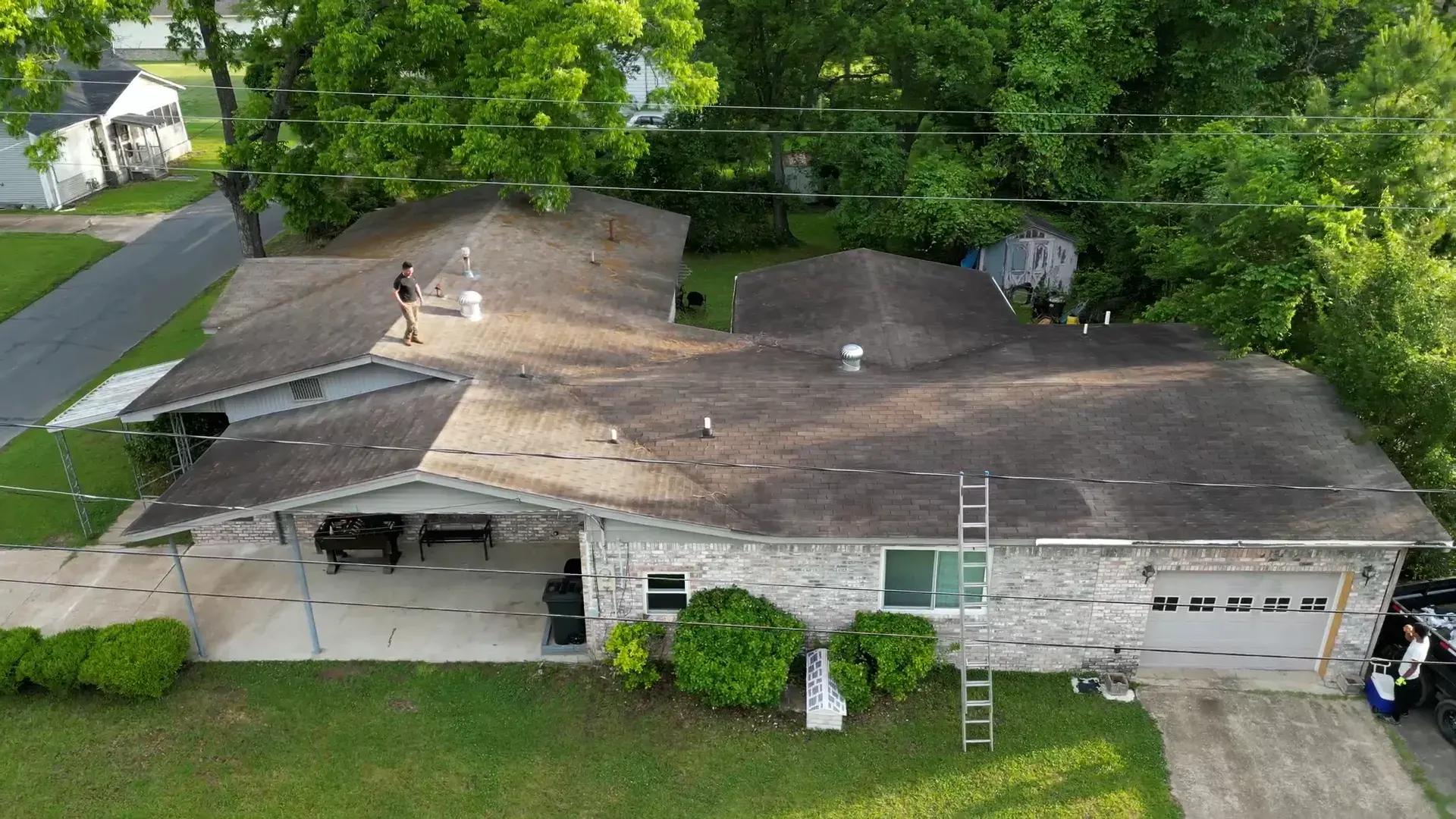 Roofer walking an aging, algae-streaked shingle roof on a brick ranch home