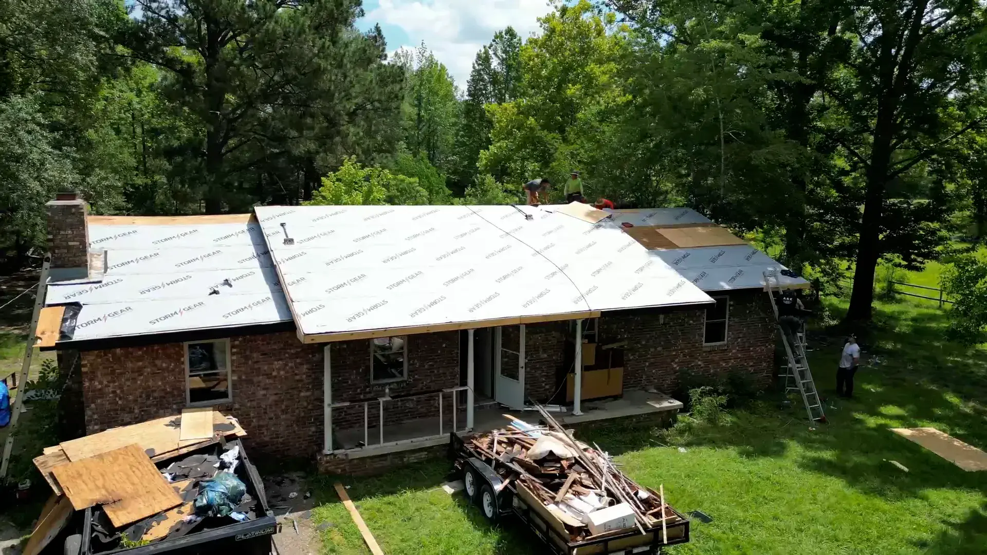 Brick ranch home mid-project with synthetic underlayment down and a tear-off trailer in the drive