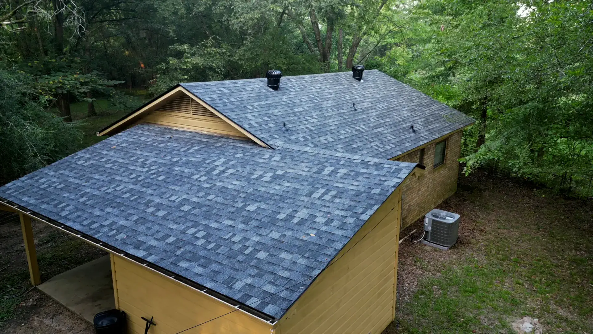 Finished gray shingle roof with turbine vents on a shaded, wooded residential lot