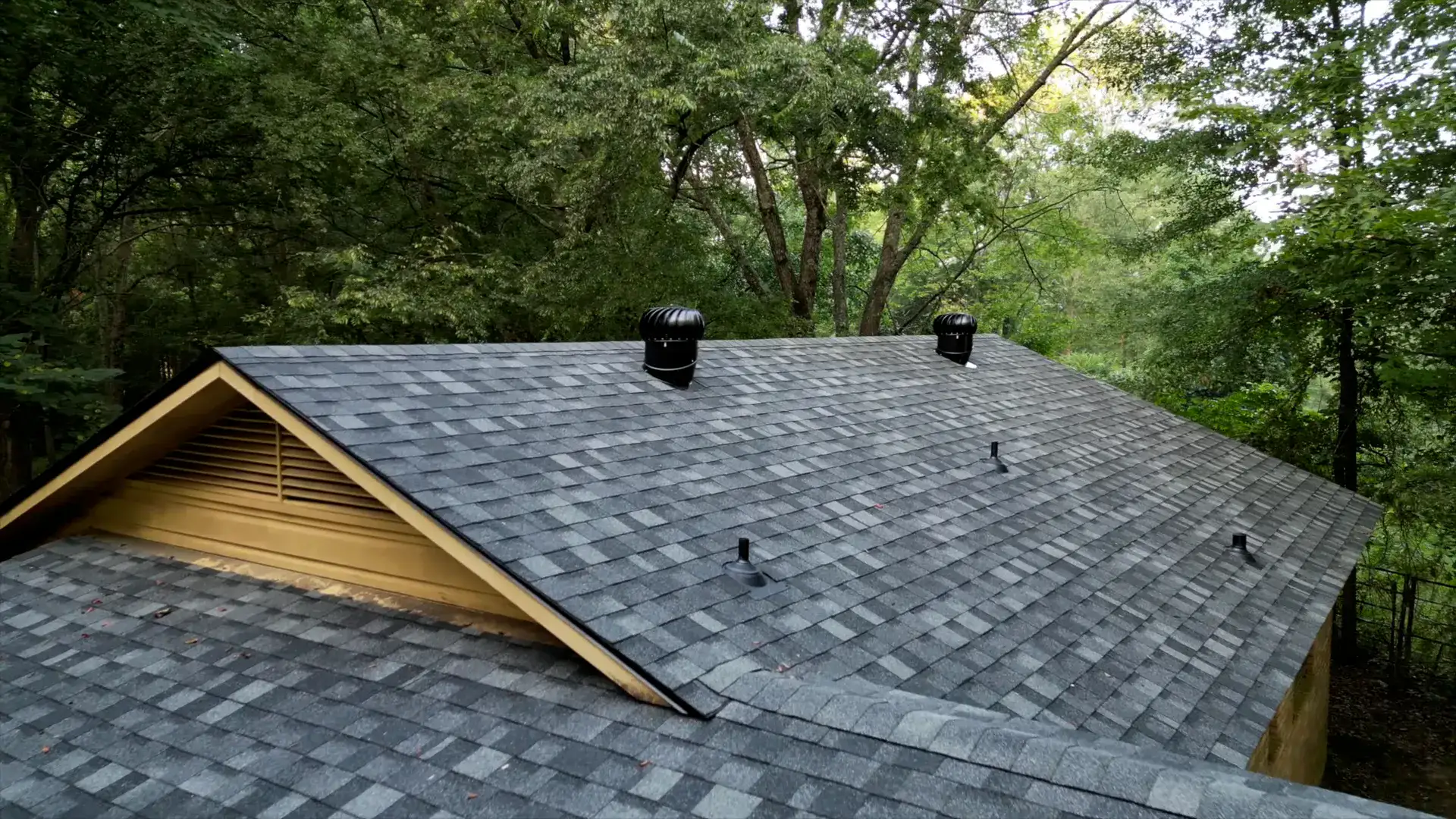 Finished gray shingle roof with ridge and turbine vents on a home surrounded by Gurdon timber