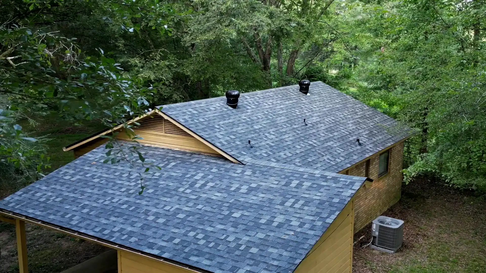 Ridge and turbine vents installed along the peak of a wooded-lot home to dry the roof deck