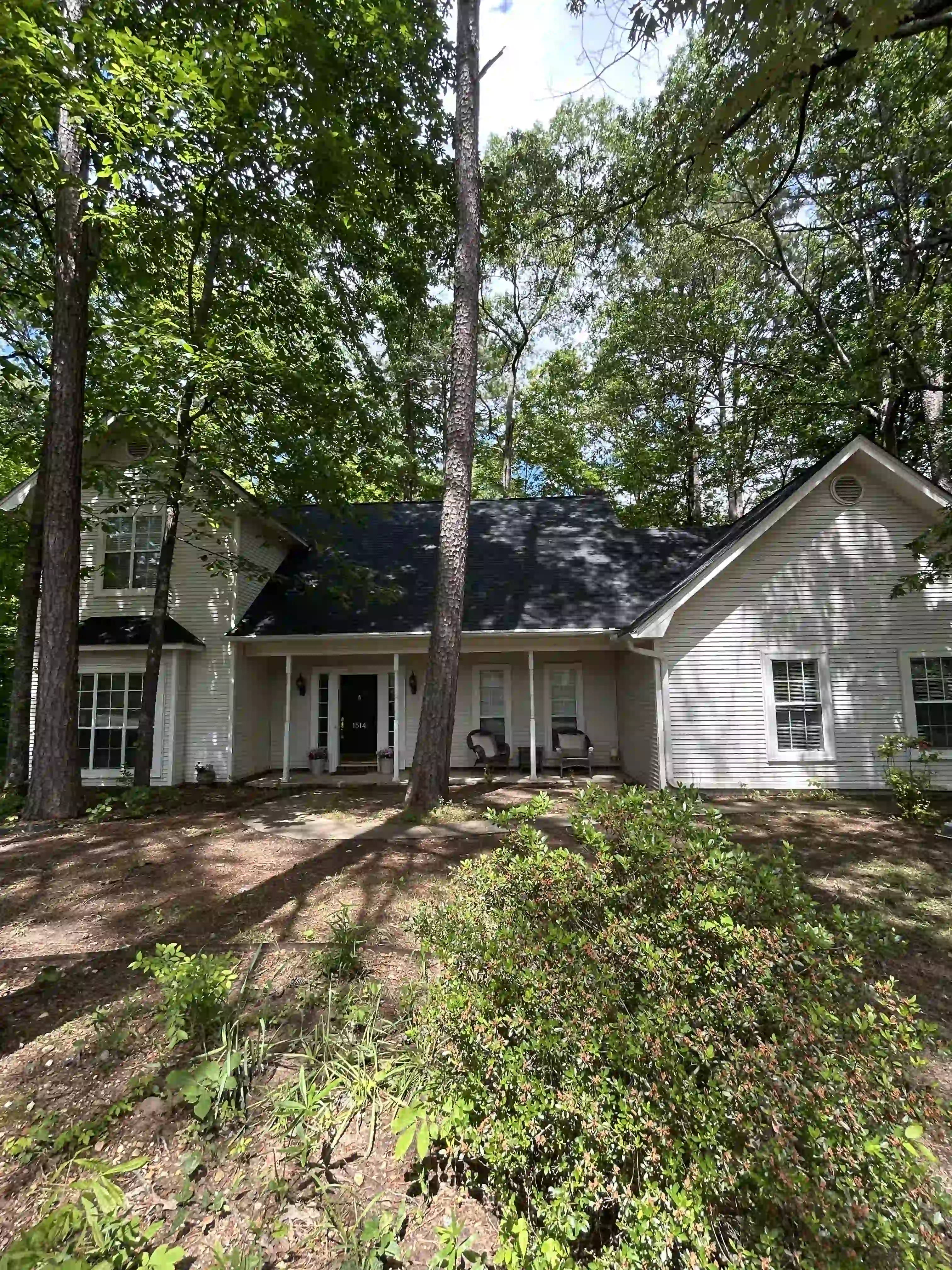 Two-story home under tall pines with the roof stripped to underlayment and debris cleared from the yard
